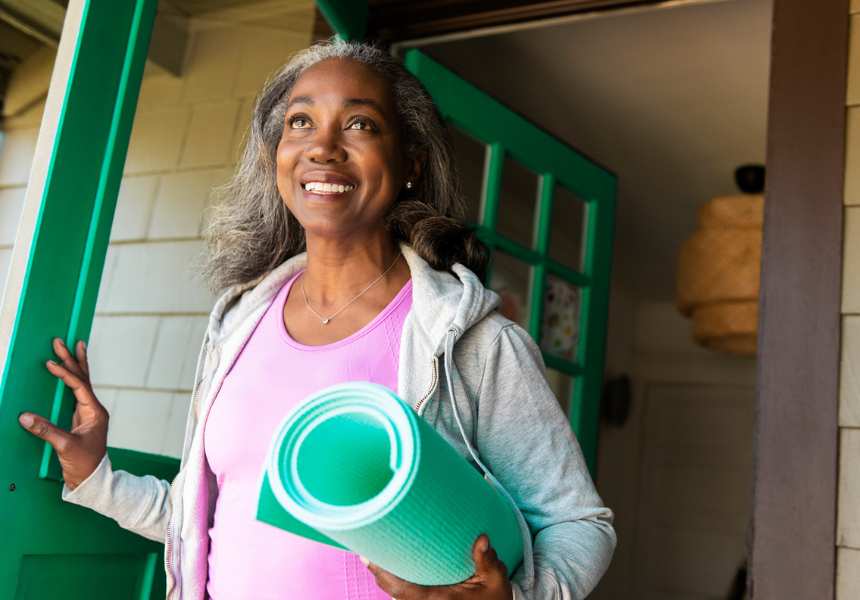 A smiling woman carries a yoga mat, symbolizing fitness and well-being in retirement, and the knowledge gained from the Retirement Resource Center to enjoy it