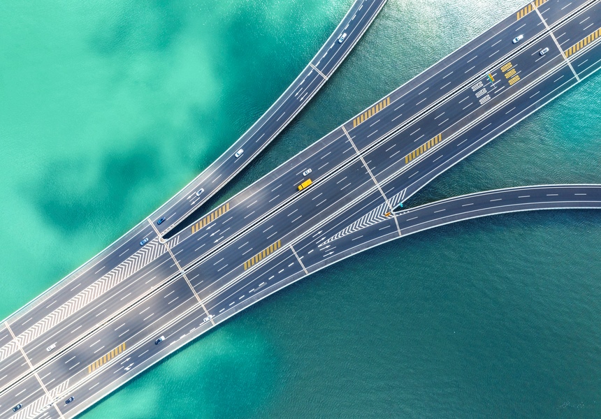 An aerial photo shows a handful of cars driving over water on a multi-lane highway that diverges in three directions.