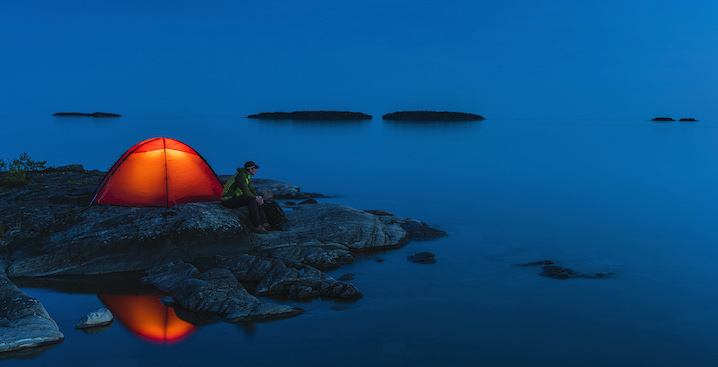 Man staring into water next to lit tent